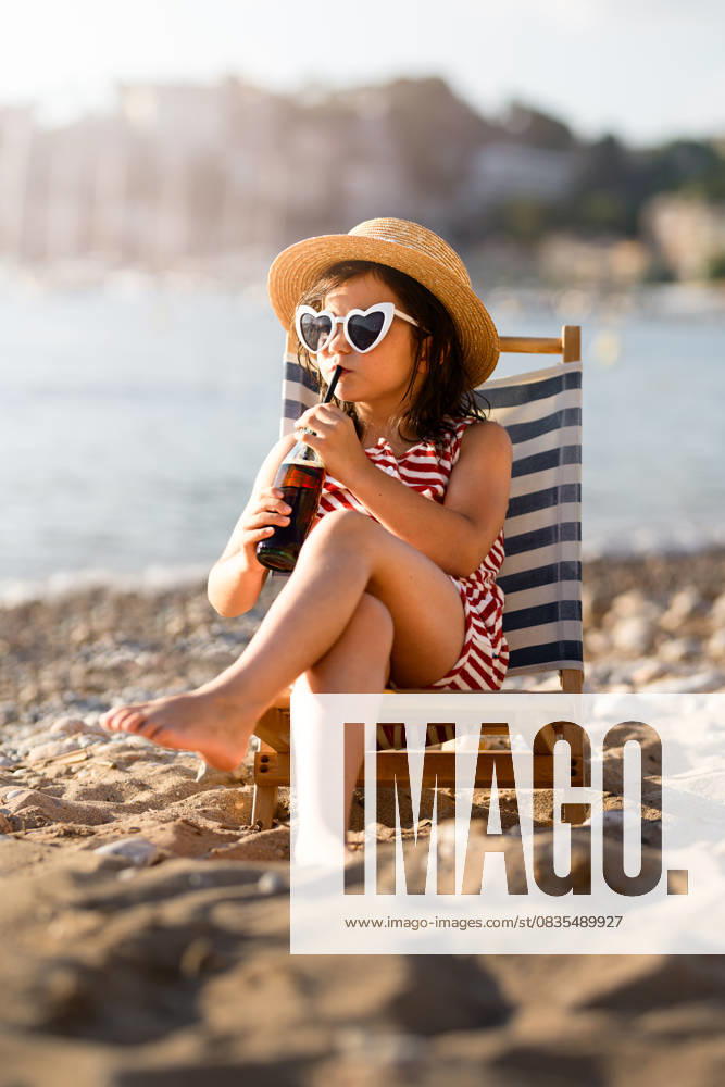 MR_ID31274_22583_MayaBosquetCarli.jpg, MR_ID31274_22584_LeoBosquetCarli.jpg A cute little girl in swimwear and heart shaped sunglasses, relaxing on a striped beach chair while sipping a drink through a straw. She s enjoying the summer sun and sandy beach scene. Model Released MagdalenaCarli_ID31274_1062185_001