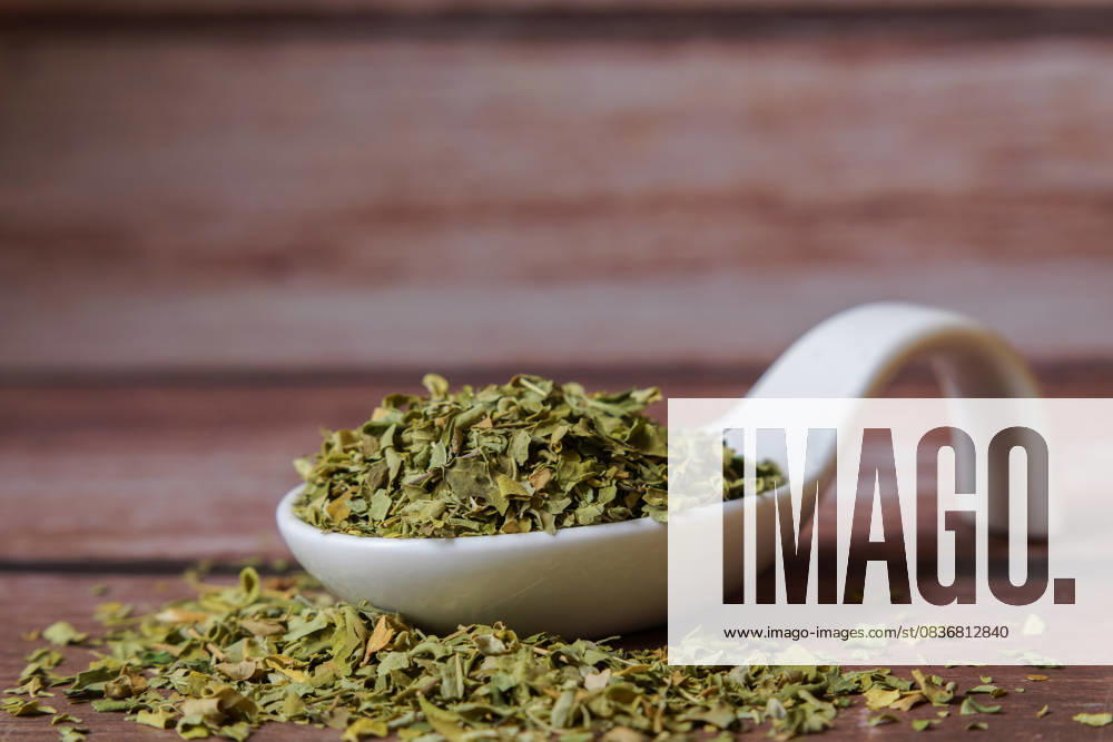 Getrocknete Moringa-Oleifera-Blätter, die einen weißen Porzellanlöffel auf einem Holztisch füllen Getrocknete Moringa-Oleifera-Blätter, die einen weißen Porzellanlöffel auf einem Holztisch füllen (License=RF)