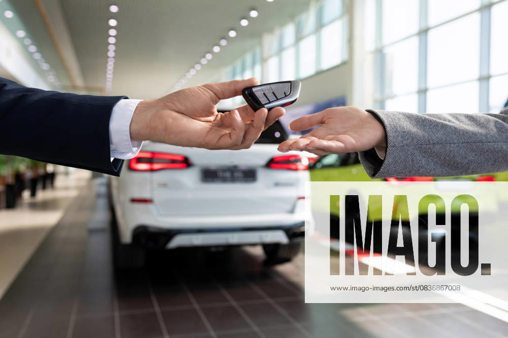 Übergabe der Schlüssel in Großaufnahme durch den Verkäufer des Autohauses an den Käufer vor dem Hintergrund von Neuwagen handing over the keys close-up by the seller of the car dealership to the buyer on the background of new cars. (License=RF) ,model released, Symbolfoto