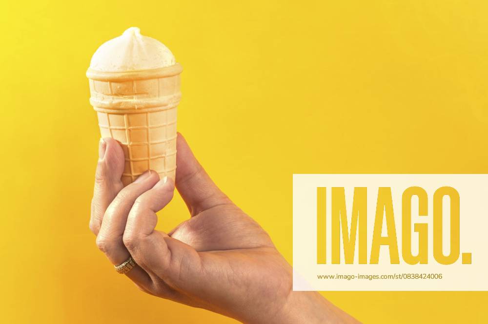 Waffelbecher mit Eiscreme in der Hand auf gelbem Hintergrund Waffle cup with ice cream in hand on yellow background