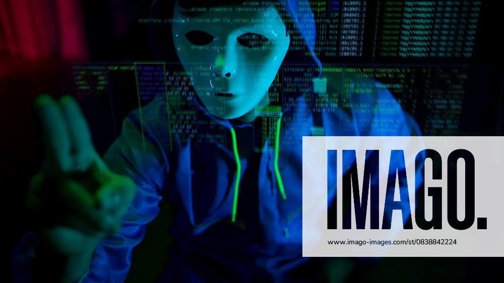 Anonymer Hacker mit Maske und Kapuze, der in einem dunklen Raum mit digitalen Daten interagiert Anonymous hacker wearing a mask and hoodie interacting with digital data in a dark room, representing cybercrime and online security threats (License=RF) ,model released, Symbolfoto
