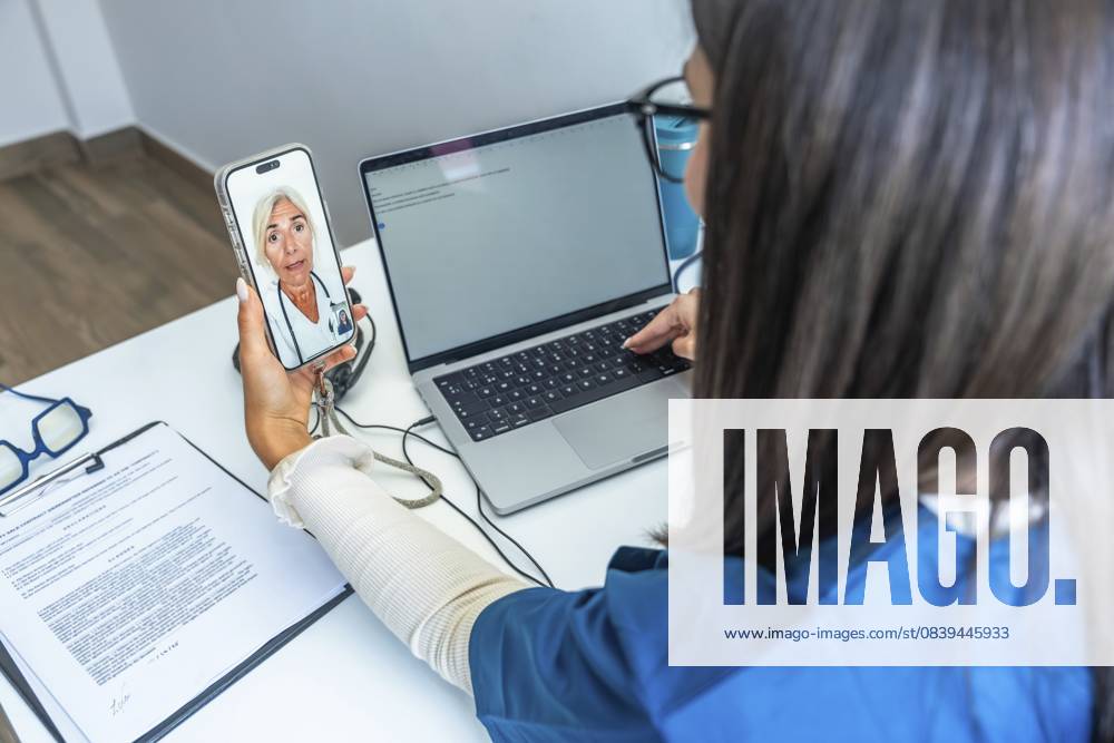 Medizinisches Fachpersonal, das auf einem Smartphone eine Videokonferenz mit einem Arzt abhält und dabei einen Laptop benutzt, um moderne Telegesundheitsdienste und digitale medizinische Kommunikation darzustellen Healthcare professional having a video conference with a doctor on a smartphone while using a laptop, representing modern telehealth services and digital medical communication