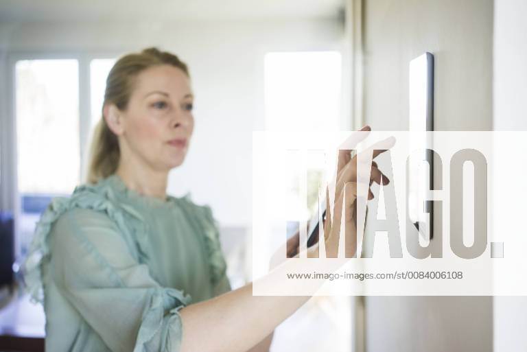 Woman adjusting digital tablet mounted on wall with smartphone model released Symbolfoto property released MOEF01056