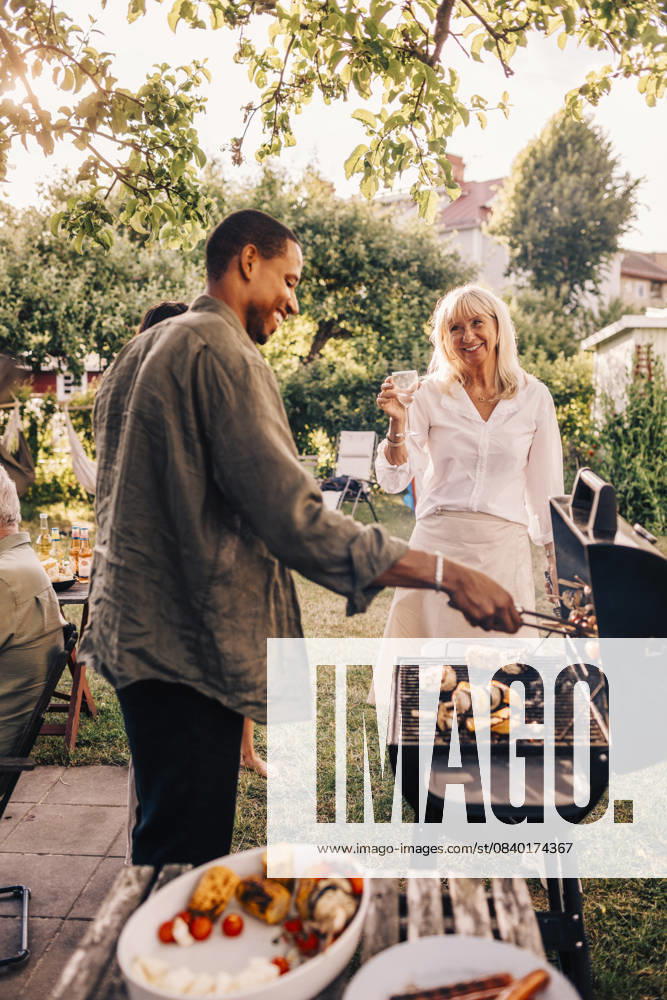 IMAGO Creative, Lifestyle, Feste im Garten #2 Happy man barbecuing while talking with mother in back yard at dinner party Sweden, Stockholm, model released