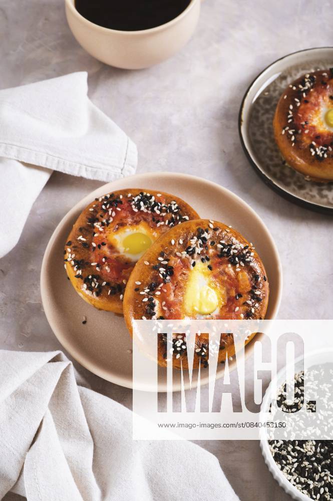 IMAGO Creative, Food, High Protein Frühstück Ei mit Tomaten und Sesamsamen, gebacken in Bagels auf einem Teller auf dem Tisch, vertikale Ansicht Egg with tomato and sesame seeds baked in bagels on a plate on the table vertical view