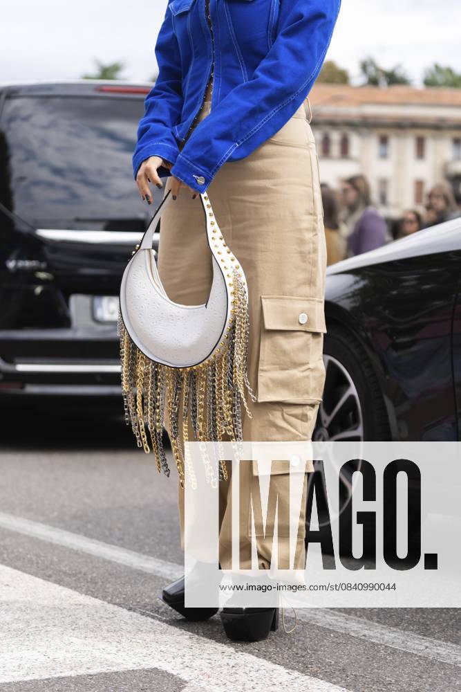 Mailand, Italien 21. September 2022: Frau in asymmetrischer Kurzjacke aus blauem Denim, Ledertasche mit genagelten Nieten, Kettenanhänger, Schulter, beigefarbene Cargo Schlaghose, Plateauschuhe mit hohen Absätzen Milan, Italy - September, 21, 2022: woman in blue denim asymmetric cropped jacket, leather bag with nailed studded fringed chain pendant shoulder, beige cargo flared pants, platform high heels shoes