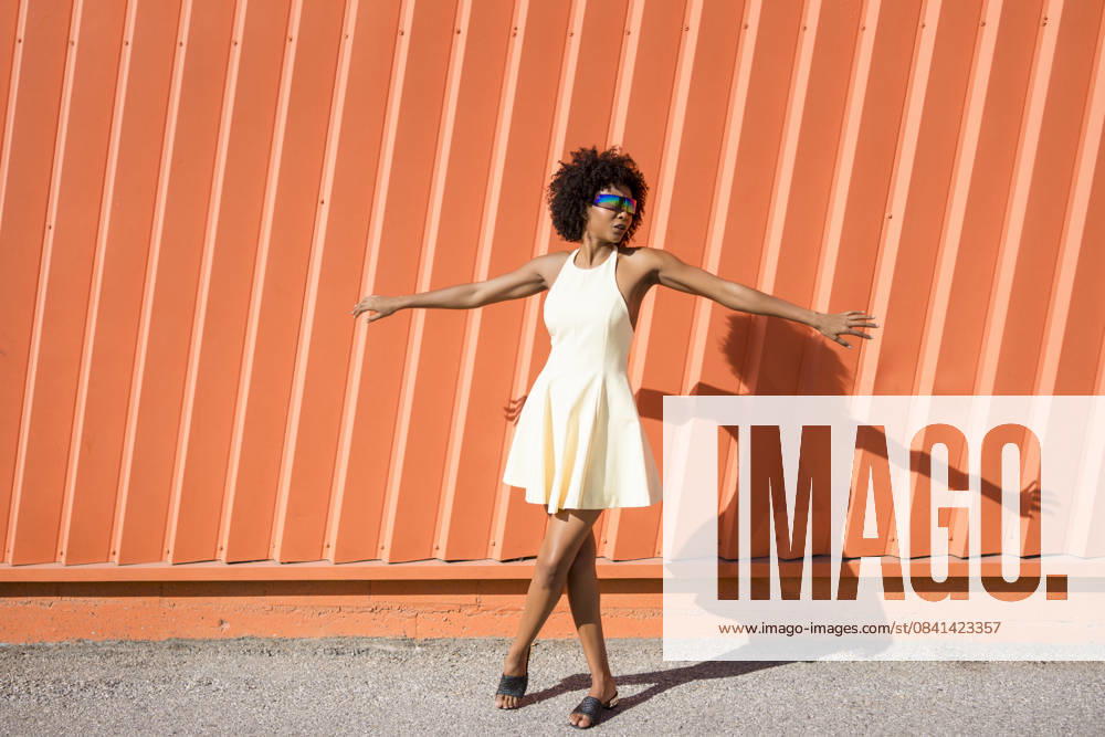 Happy woman with afro hairstyle in yellow dress dancing by orange wall model released, Symbolfoto, JSMF03464