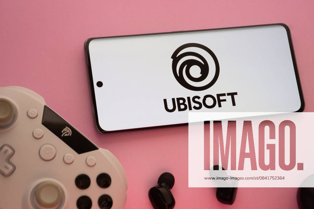 Dhaka, Bangladesch - 22. März 2025: Smartphone mit Ubisoft-Logo, Game-Controller und Ohrstöpsel auf einem rosa Hintergrund. Dhaka, Bangladesh- 22 Mar 2025: Smartphone with Ubisoft logo, game controller, and earbuds on a pink background. (License=RM)