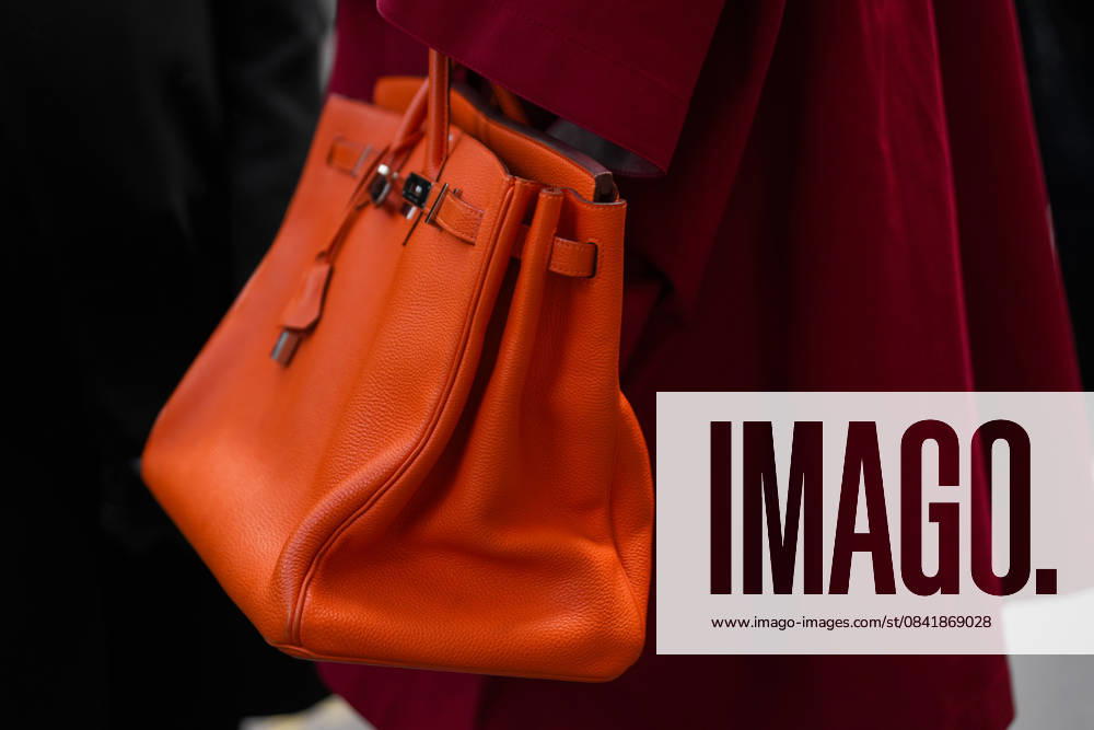 Paris, Frankreich - 4. Oktober 2025: Ein Mann trägt eine orangefarbene Birkin-Tasche von Hermes. Mode Outfit Handtasche Details, Street Style Look Paris, France - October, 4, 2025: Man wears Hermes orange Birkin bag. Fashion outfit handbag details, street style look accessories, luxury leather accessory (License=RM)