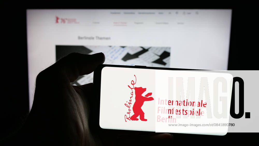 Illustration in Germany. In this photo illustration, a person is holding a mobile phone with the logo of Berlin International Film Festival Berlinale on screen in front of web page. Germany