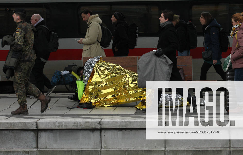 A homeless man lies on a bench on the platform at Hamburg Central Station Travelers walk past him St Georg Hamburg