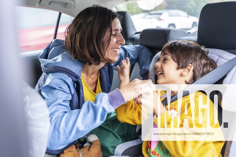Mutter dreht sich zu ihrem Sohn zurück, sitzt in einem Kindersitz, teilt freudige Momente und lacht während einer schönen Autofahrt und stärkt ihre Verbundenheit durch Liebe und Zusammengehörigkeit Mother turning back to her son, sitting in a child car seat, sharing joyful moments and laughter during a delightful car trip, strengthening their bond through love and togetherness