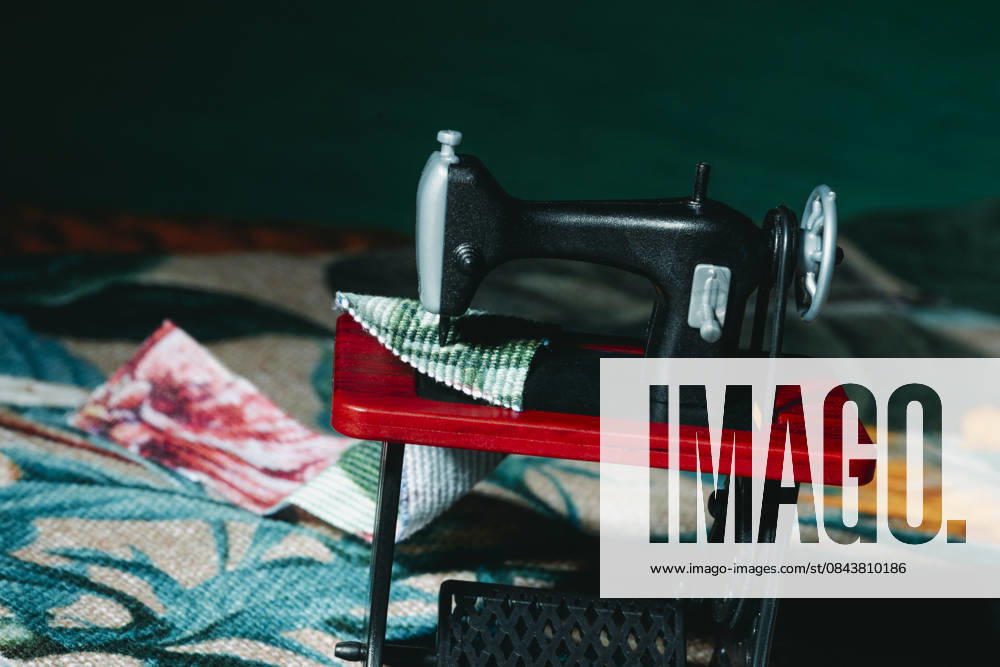 IMAGO Creative, Lifestyle, Freizeit, Hobby, Handarbeit, Nähen #2 Toy sewing machine working with fabric on bold red tabletop, JMYF00185
