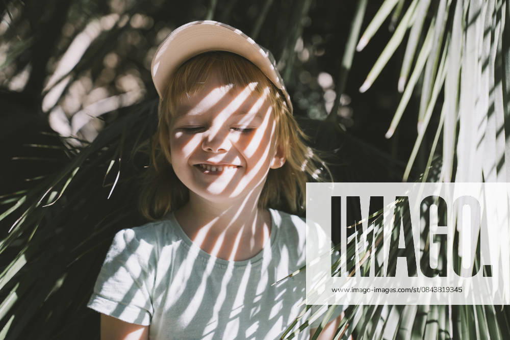 Playful child hiding behind palm leaves outdoors in sunlight model released, Symbolfoto, NDEF03045