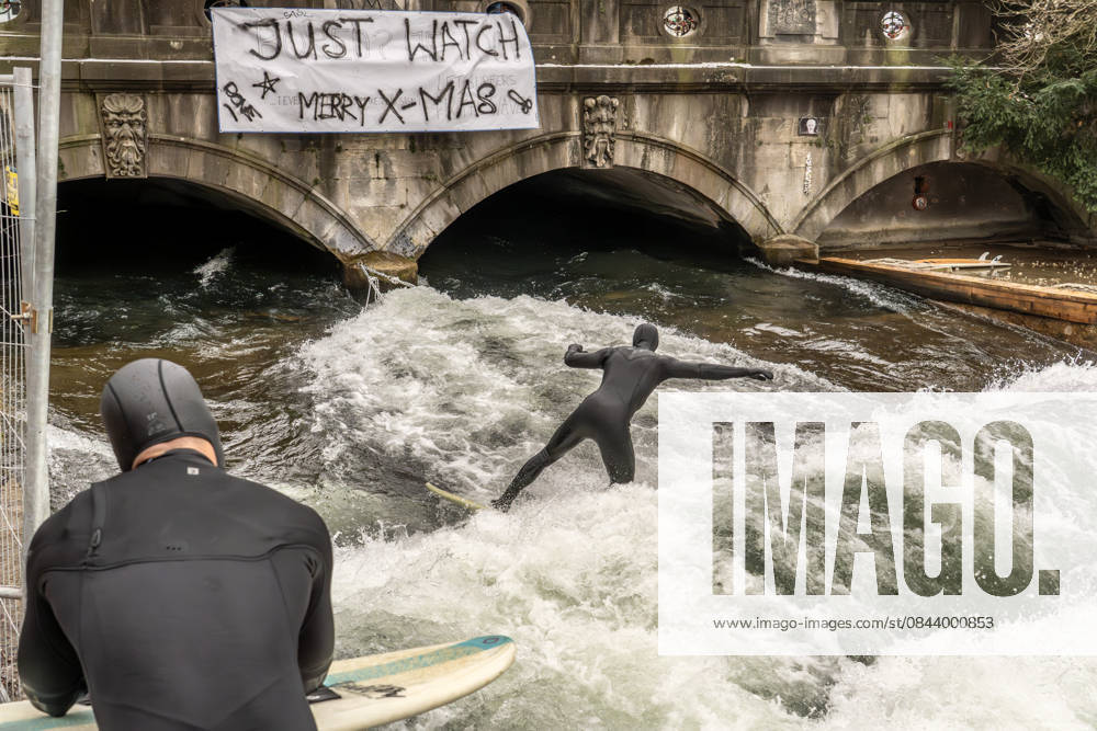 Eisbachwelle ist an Weihnachten zurück, ein Weihnachtswunder, seit Wochen war Stillstand, nun haben sich die Surfer selbst geholfen, provisorisch ein Brett ins Wasser gehängt, die Surfer sind glücklich, München, 26. Dezember 2025 Deutschland, München, 26. Dezember 2025, die Eisbachwelle ist zurück, seit gestern können wieder Surfer auf der Welle surfen, die berühmte Eisbachwelle wurde von den Surfern heimlich selber repariert, zwei Seile sind an der Brücke befestigt, dazwischen hängt ein Brett, das unter Wasser für den nötigen Widerstand sorgt und damit die neue alte Surfwelle aufbaut, Transparent an der Brücke: Just Watch, Merry X-mas , ein Weihnachtswunder, eine große Überraschung zu Weihnachten, seit fast zwei Monaten war
