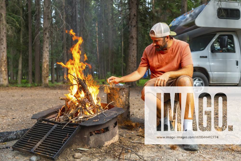 Tourist, der Lagerfeuerflammen in der Nähe eines Wohnmobils im Banff Nationalpark, Kanadische Rocky Mountains, Alberta, füttert und ein friedliches Campingerlebnis inmitten der Natur genießt Tourist feeding campfire flames near camper van in banff national park, canadian rockies, alberta, enjoying peaceful camping experience surrounded by nature