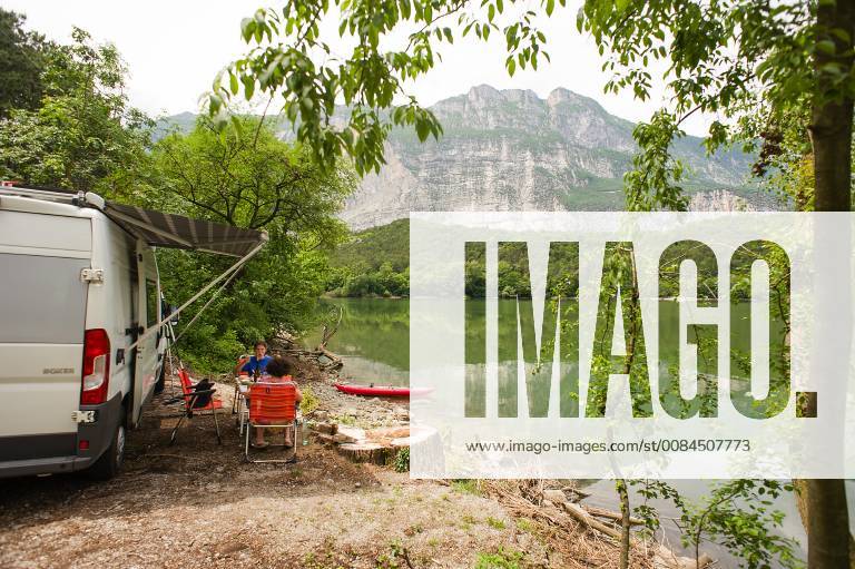 Rest in a motorhome and kayak on the shores of Lake Garda Lago di Cavedine in the province of Trento Trentino Italy A motorhome with a kayak stands on the shore of a lake with a set table and chairs