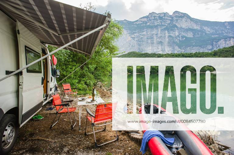 Rest in a motorhome and kayak on the shores of Lake Garda Lago di Cavedine in the province of Trento Trentino Italy A motorhome with a kayak stands on the shore of a lake with a set table and chairs