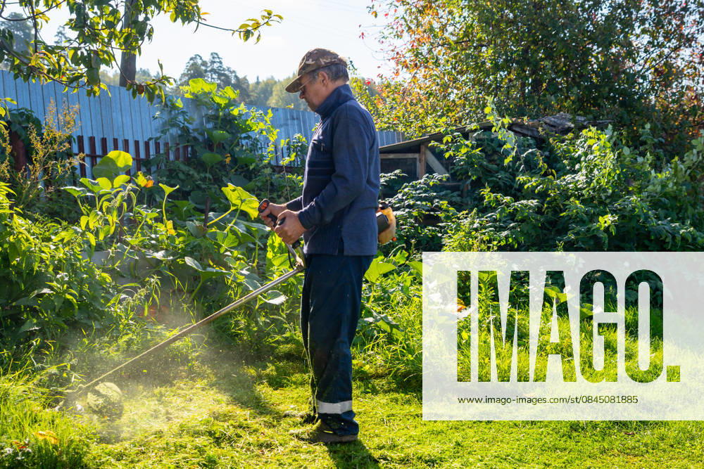 Senior man uses grass trimmer to cut overgrown lawn in his backyard Chelyabinsk, Chelyabinsk Oblast, Russia CR_STCJ260106-1921651-01 ,model released, Symbolfoto