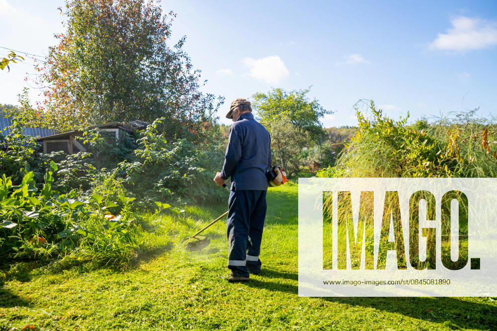 Senior man uses grass trimmer to cut overgrown lawn in his backyard Chelyabinsk, Chelyabinsk Oblast, Russia CR_STCJ260106-1921652-01 ,model released, Symbolfoto