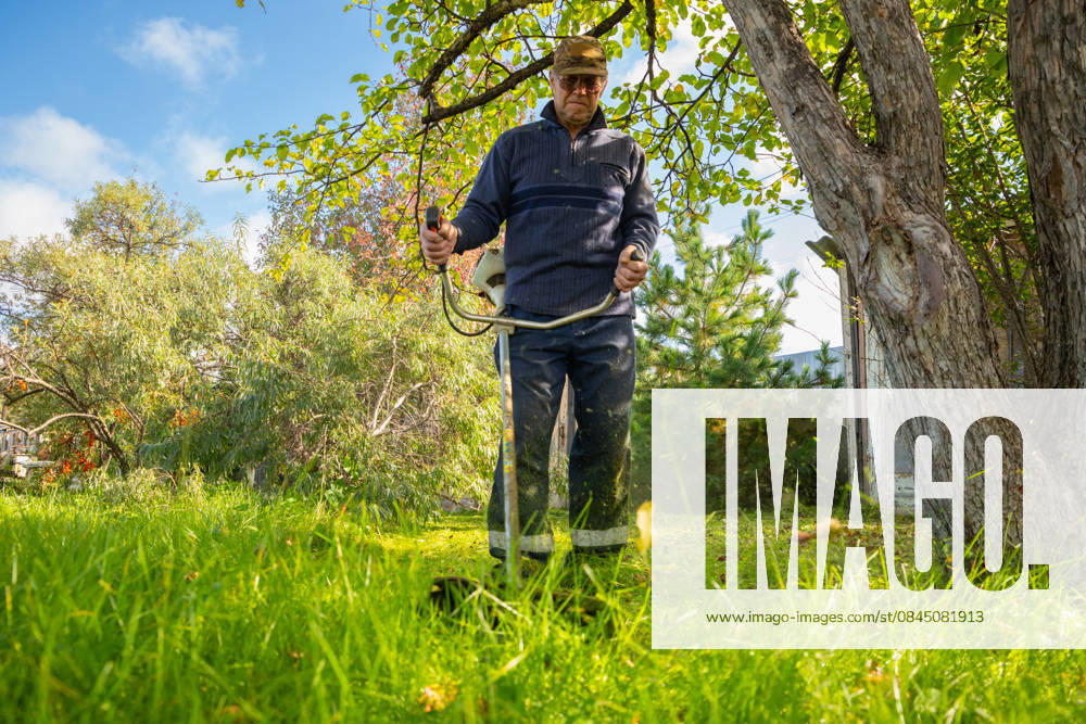 Senior man uses grass trimmer to cut overgrown lawn in his backyard Chelyabinsk, Chelyabinsk Oblast, Russia CR_STCJ260106-1921672-01 ,model released, Symbolfoto