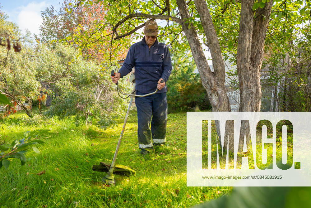 Senior man uses grass trimmer to cut overgrown lawn in his backyard Chelyabinsk, Chelyabinsk Oblast, Russia CR_STCJ260106-1921673-01 ,model released, Symbolfoto