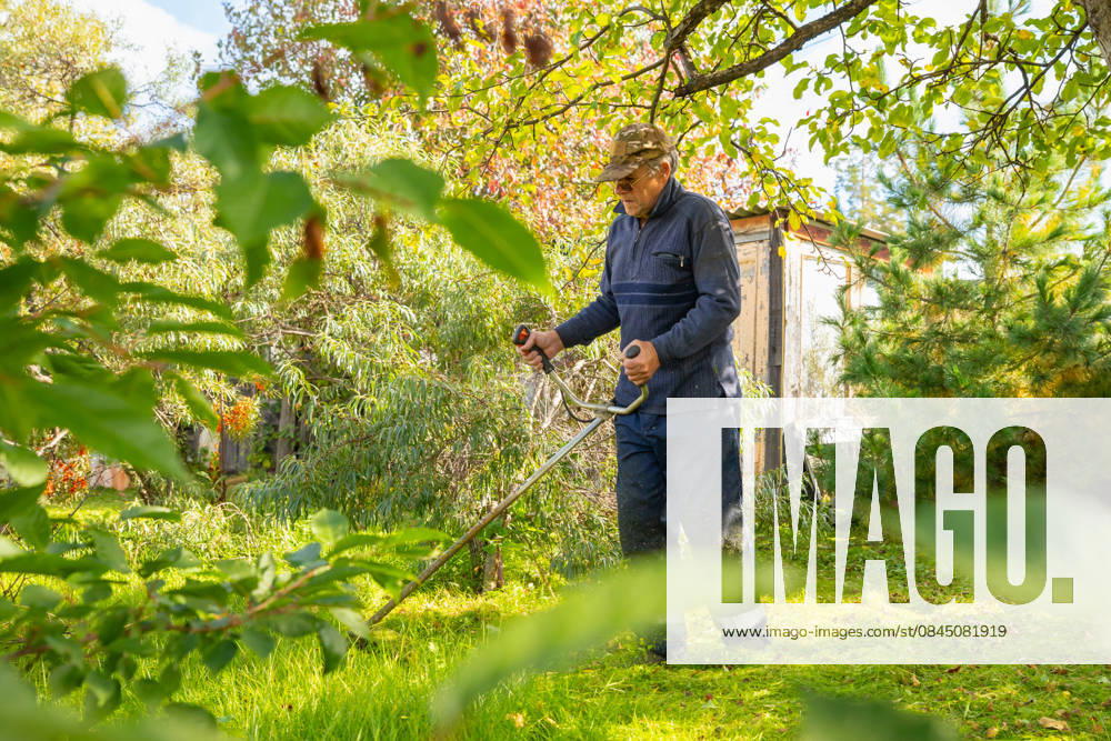 Senior man uses grass trimmer to cut overgrown lawn in his backyard Chelyabinsk, Chelyabinsk Oblast, Russia CR_STCJ260106-1921678-01 ,model released, Symbolfoto