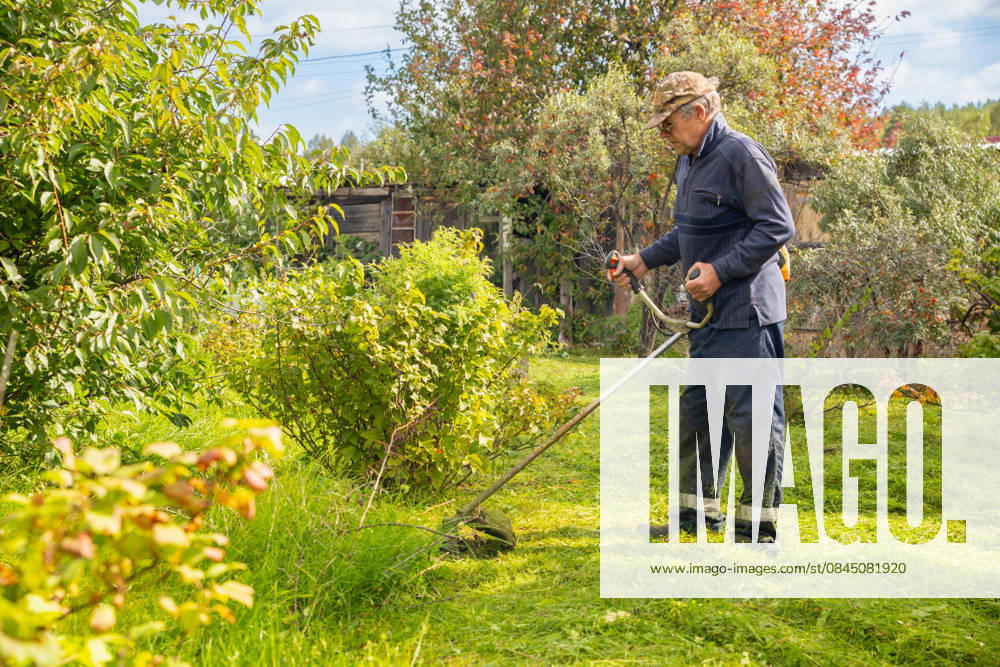 Senior man uses grass trimmer to cut overgrown lawn in his backyard Chelyabinsk, Chelyabinsk Oblast, Russia CR_STCJ260106-1921693-01 ,model released, Symbolfoto