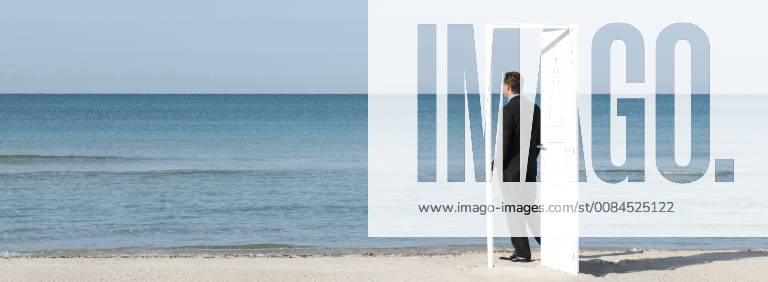 Businessman standing on beach looking at ocean, seen through open door