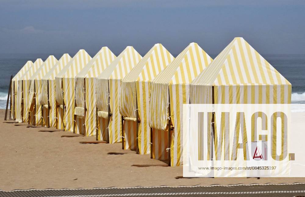 Region Aveiro - Portugal Gelb und weiß gestreifte Strandzelte an der Küste Stripe beach tents standing in a row on sand with sea in background (License=RF)