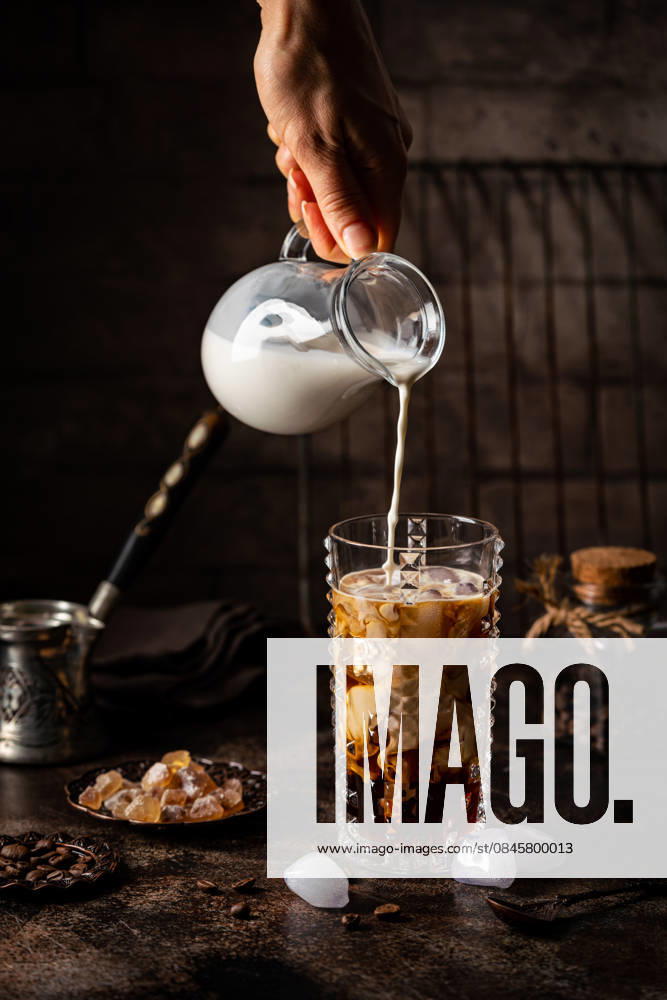 Eiskaffee in einem hohen Glas Ice coffee in a tall glass with cream poured over, sugar and coffee beans on dark background (License=RF)