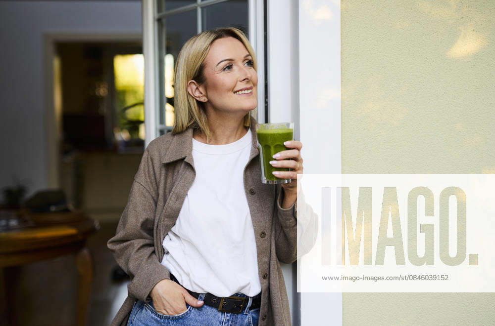 Smiling person with green smoothie standing on the patio at home model released, Symbolfoto property released, BSZF02945