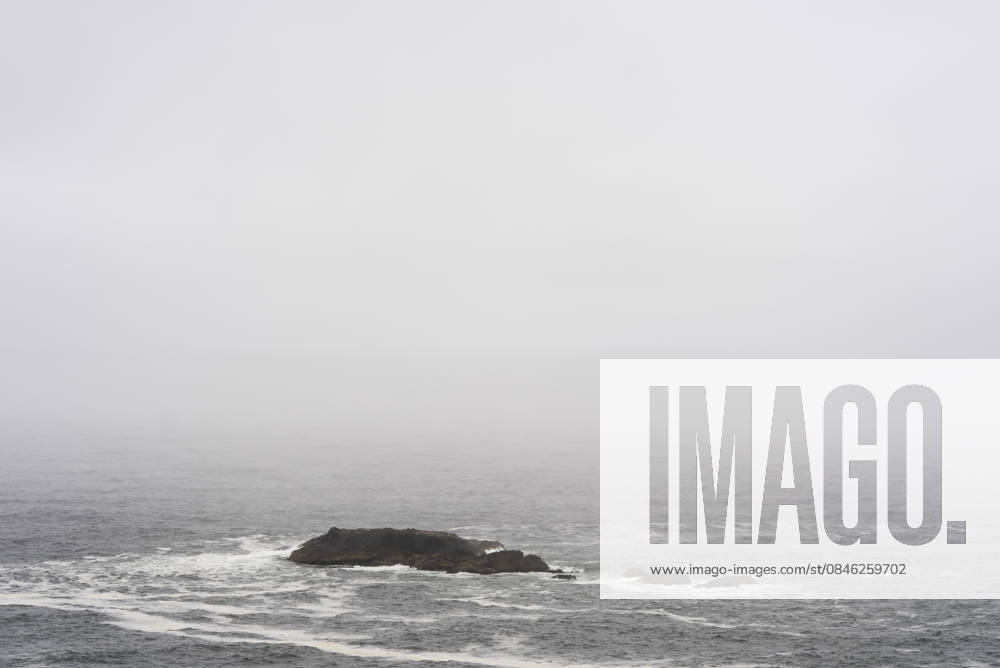 Coastal landscape with small rock in the fog on Chiloe Chile, Patagonia gray sea with low waves dark rocks small island in the haze Chiloe, 15 12 2025 Chiloe Chile