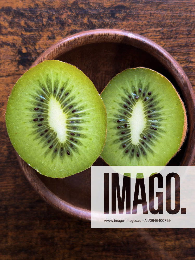 Kiwi-Frucht-Hälften in Holzschale, Draufsicht Top view of fresh green kiwi sliced in half inside a rustic wooden bowl, showing vibrant texture, seeds, and healthy tropical fruit concept. (License=RF)