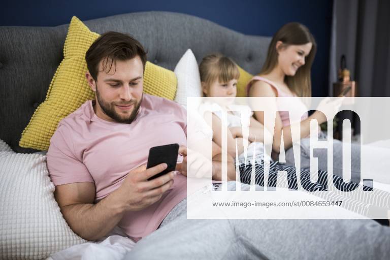 Neglected little girl sitting on bed with her parents, using smartphones model released Symbolfoto property released AWF00043