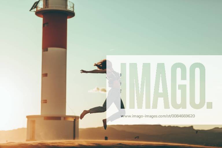 Young woman jumping in desert landscape at lighthouse model released Symbolfoto OCAF00275
