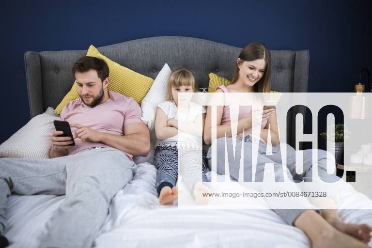 Neglected little girl sitting on bed with her parents, using smartphones model released Symbolfoto property released AWF00042
