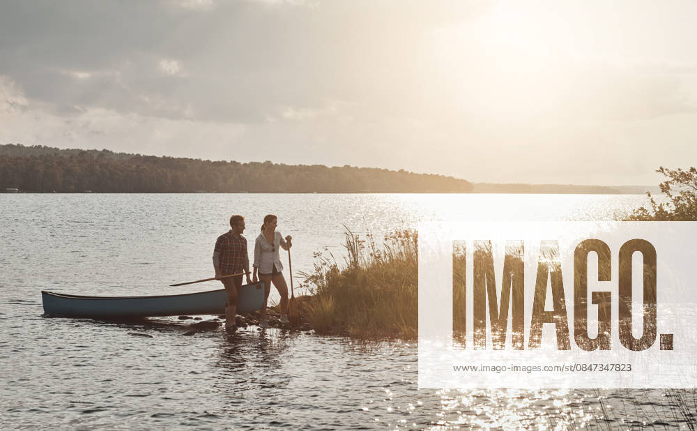 Couple, date and travel with canoe, lake and people on adventure, bonding and love on summer holiday. Outdoor, man and woman with boat on water, romance or together in nature, sunshine and space. model released property released