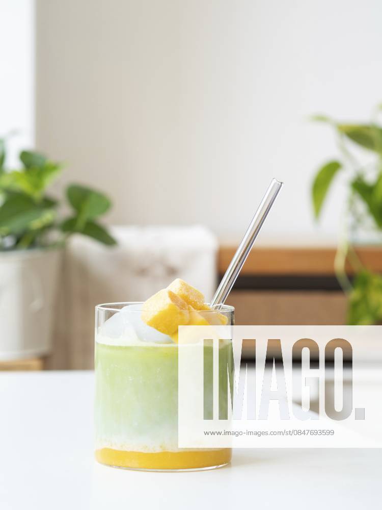 Gefrorener Matcha Latte mit tropischer Mango, Milch und klarem Strohhalm in einem Glas Iced matcha latte with tropical mango, milk, and clear straw in a glass