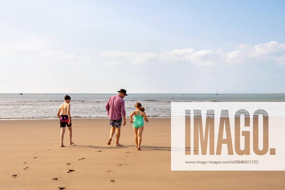 Back view of single father with kids walking on beach to the sea. Wales, England, United Kingdom R_JNDO260222-1935004-01 ,model released, Symbolfoto