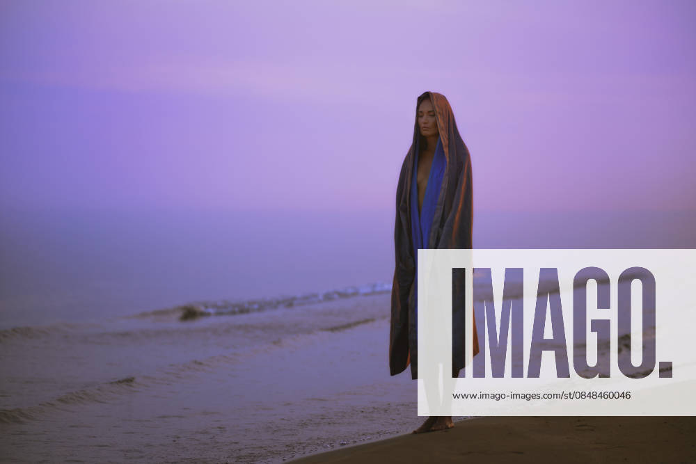 Woman in robe standing on coastline at sunrise in contemplative mood model released, Symbolfoto property released, AZF01134
