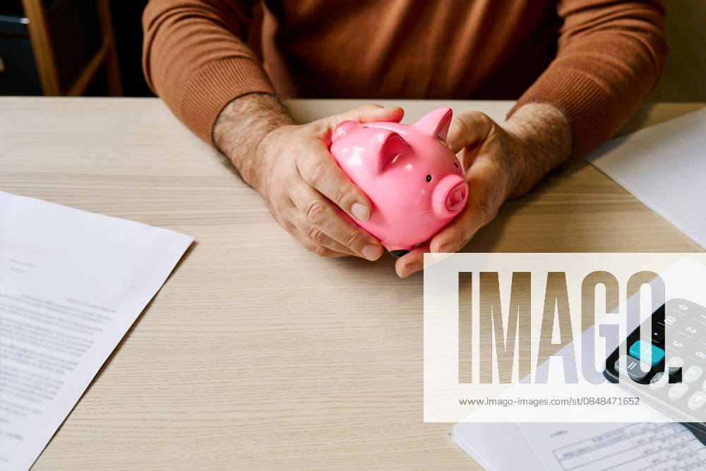 Man holding piggy bank at table with bills and calculator at home model released, Symbolfoto property released, CATF00870