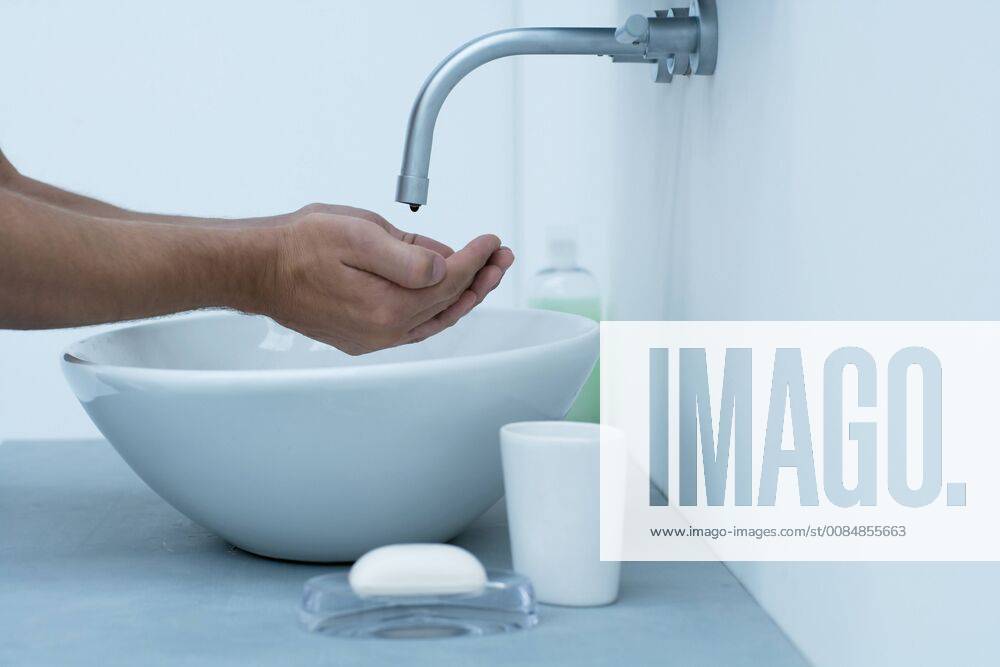 Man holding hands under dripping faucet in bathroom sink, cropped