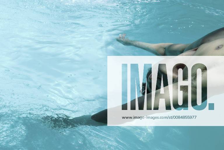 Man leaning backward over swimming pool, dangling arms in water