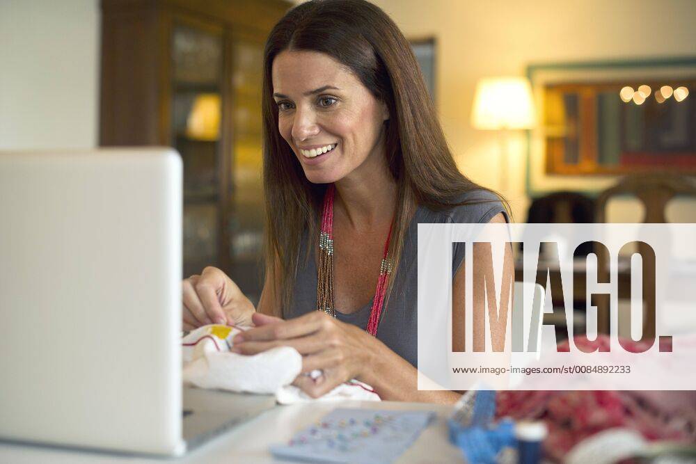Woman looking at laptop computer while sewing