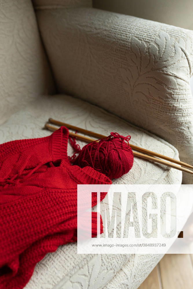 Knitting hobby with red sweater on comfortable armchair A plush armchair displays a vibrant red sweater, knitting needles, and yarn, capturing the essence of a cozy knitting hobby Model Released Nastyaofly_ID33665_1171508_003