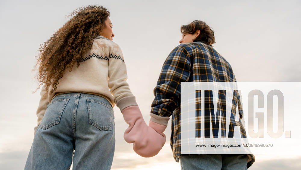 Young couple holding hands as a symbol of pride A young lesbian couple holding hands, symbolizing their love and pride. Captured from behind against a serene sky, showcasing unity and LGBT representation in a beautiful moment. Model Released SilviaRedondo_ID33866_1192396_031