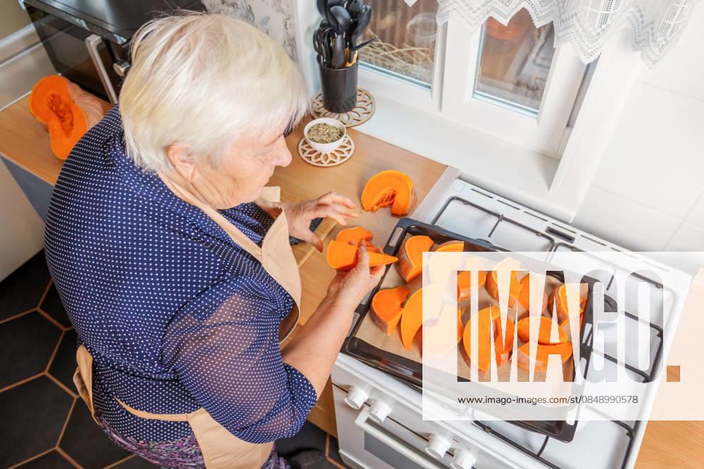 Woman preparing pumpkin for baking in kitchen A woman in her home kitchen prepares fresh pumpkin slices for baking on a tray. The cozy setting and natural light enhance the vibrant orange hues of the pumpkin pieces. Model Released SvetlanaRadayeva_ID33948_1196291_008