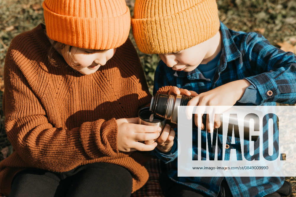 Children enjoying autumn warmth in forest adventure Two children dressed in cozy autumn attire share a warm beverage from a thermos during a forest adventure, capturing the warmth and joy of a mini journey in a lush autumn setting. Model Released ZulfiiaIshmukhametova_ID32754_1115172_011