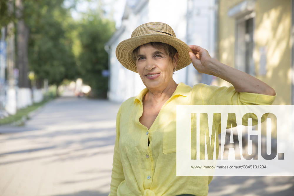 Glückliche ältere Frau mit Sonnenhut spaziert durch die Sommerstadt happy senior woman in sun hat walks on summer city (License=RF) ,model released, Symbolfoto